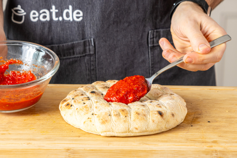 Tomatensoße auf Fladenbrotpizza verteilen