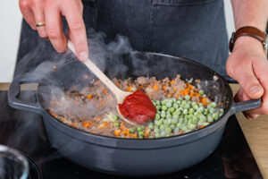Gefrorene Erbsen und Tomatenmark dazugeben