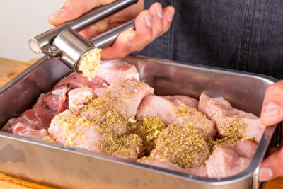 Oregano und Knoblauch zum Fleisch geben