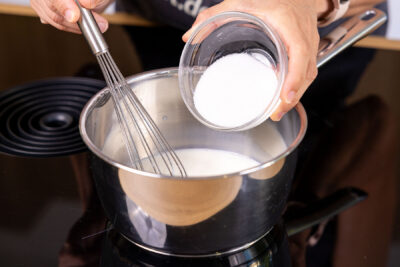 Zucker zur Milch in den Topf geben