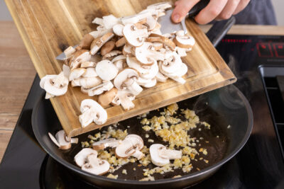 Champignonscheiben zu Zwiebel und Knoblauch in die Pfanne geben