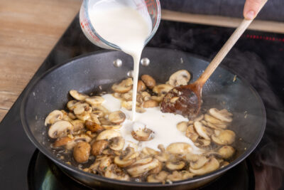 Sahne zu den Champignons in die Pfanne gießen