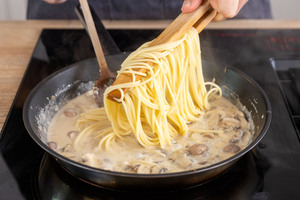 Spaghetti zur Pilzsoße in die Pfanne geben