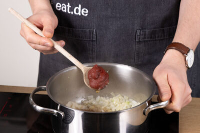 Tomatenmark mit den Zwiebeln anschwitzen.