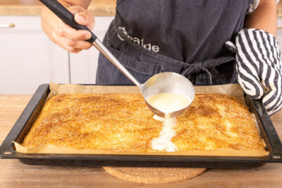 Butter-Sahne-Guss über den schneller Kuchen mit Kokosraspeln gießen