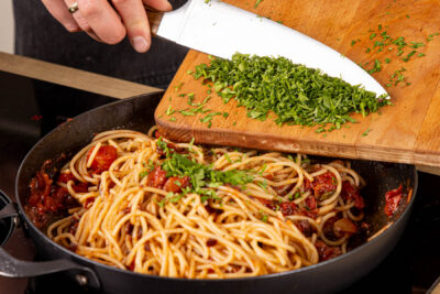 gehackte Petersilie und Spaghetti unter die Soße mengen