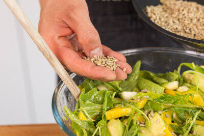 Sonnenblumenkerne über den Avocado-Mango-Salat geben