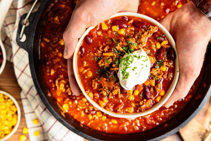 Chili con Carne aus dem Dutch Oven serviert mit gehackten Kräutern und Crème fraîche