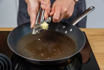 Knoblauch in die Pfanne pressen