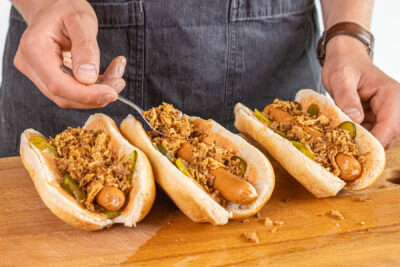 Röstzwiebeln auf den Hot Dogs verteilen