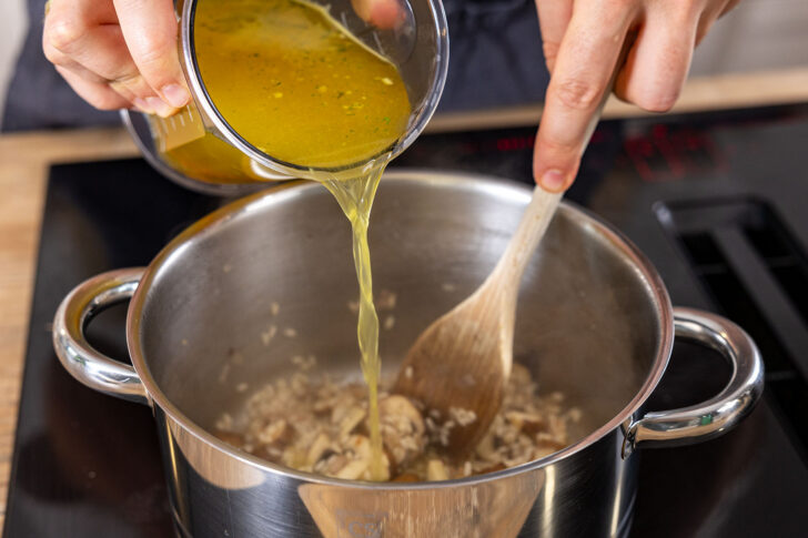 Gemüsebrühe zum Risotto mit Champignons gießen