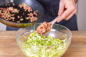 Schinkenwürfel und Zwiebel unter den Krautsalat heben