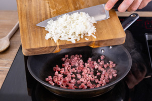 Zwiebel zu den Schinkenwürfeln in die Pfanne geben