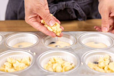 Streusel über den Blaubeermuffins verteilen
