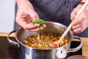 Petersilie in die vegetarische Linsensuppe geben