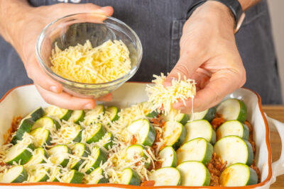 Geriebenen Käse über Zucchini verteilen