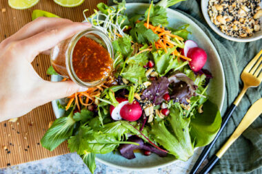 Asiatisches Salatdressing über Salat geben