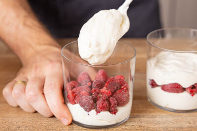 Creme und Himbeeren abwechselnd in Dessertgläser schichten