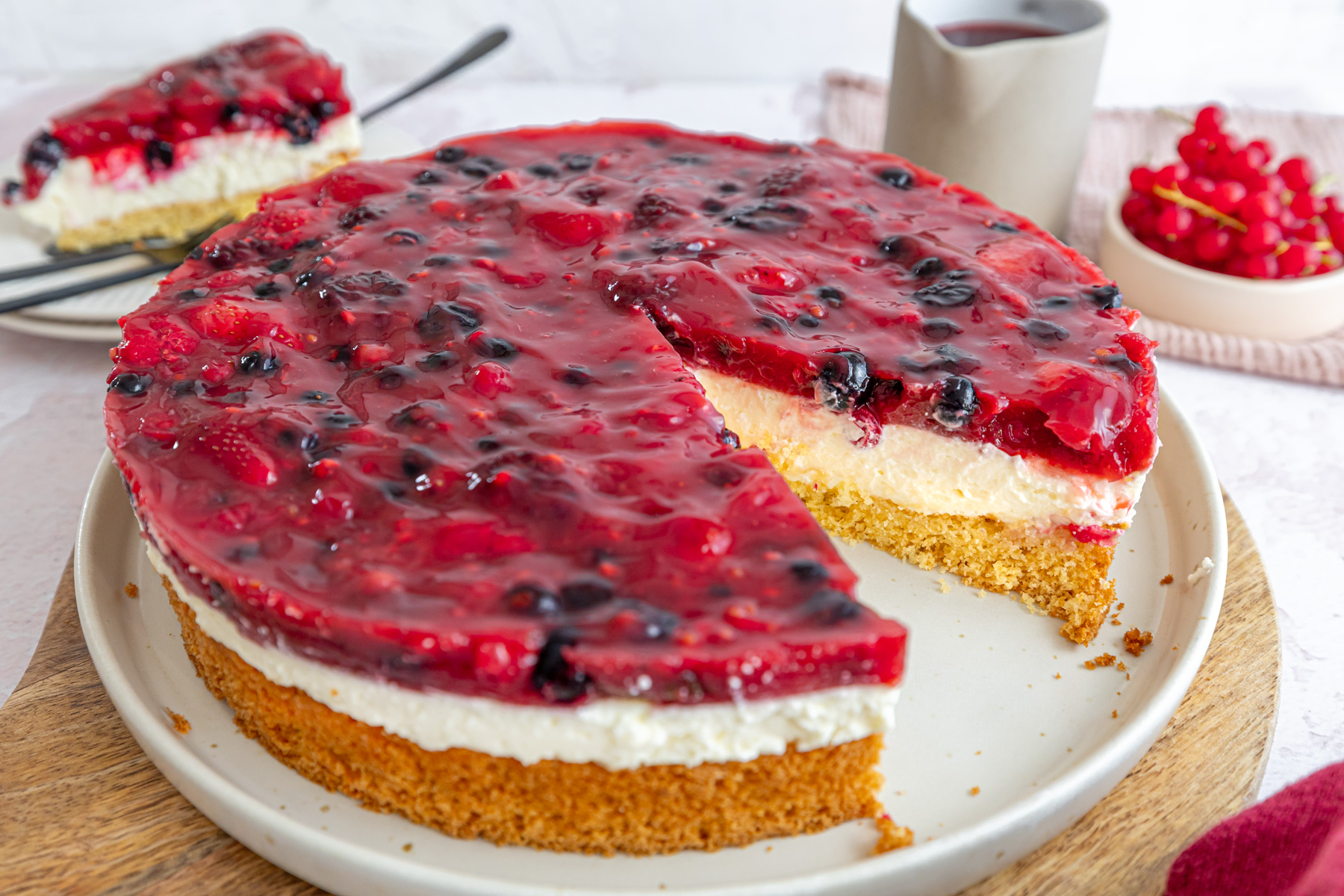 A bowl of vibrant Rote Grütze topped with fresh whipped cream and served with vanilla sauce