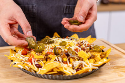 Käse und Jalapeño auf den Nachos verteilen