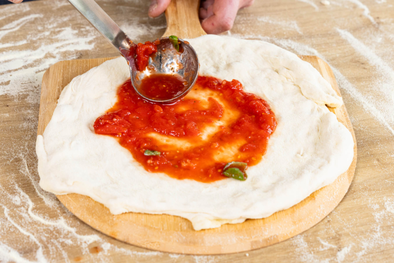 Tomatensoße auf dem Pizzaboden verteilen