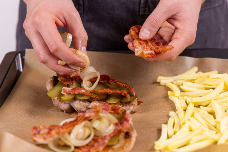 Bacon, Gurken und Zwiebeln auf den Steaks verteilen