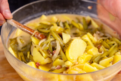 Gewürzgurkenunter bayrischen Kartoffelsalat mit Speck mengen