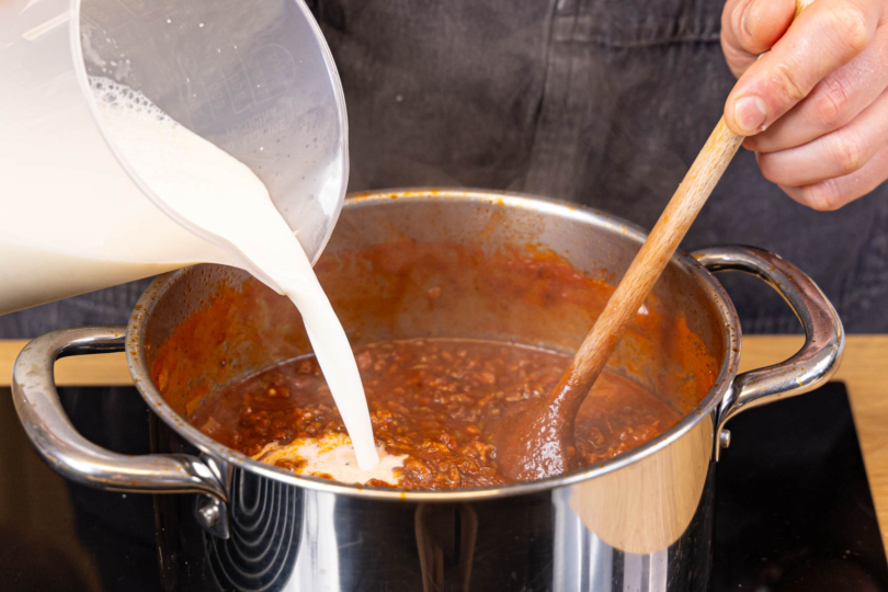 Milch zur Bolognese-Suppe gießen und kurz aufkochen