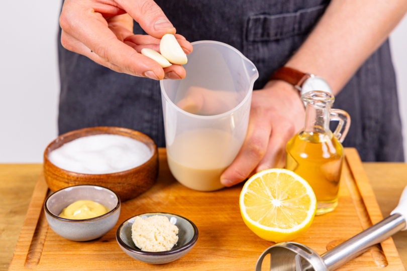 Knoblauch und weitere Zutaten für vegane Mayo mit Sojamilch in Mixbecher geben