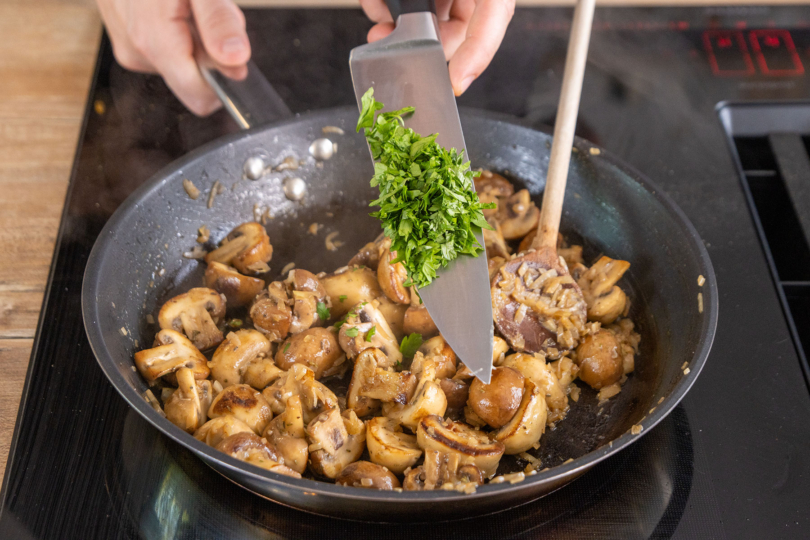 Petersilie zu den gebratenen Champignons geben