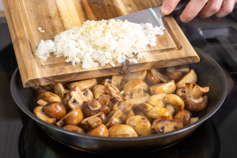 Zwiebel und Knoblauch zu den Champignons geben