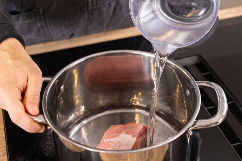 Wasser zum Fleisch in den Topf gießen