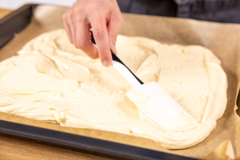 Teig für Pfirsichkuchen auf dem Blech verstreichen