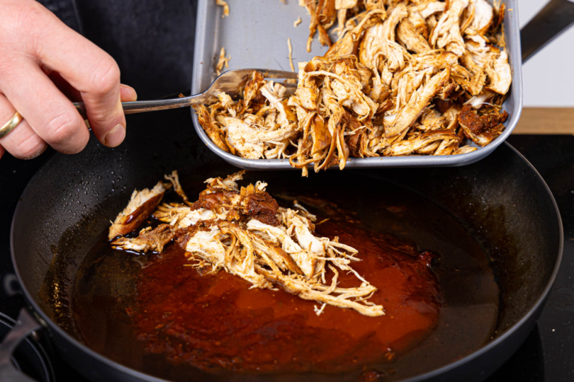 gerupftes Hähnchenfleisch in die BBQ-Sauce geben