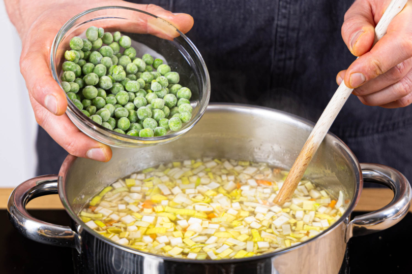 Erbsen in die Nudelsuppe geben und köcheln lassen