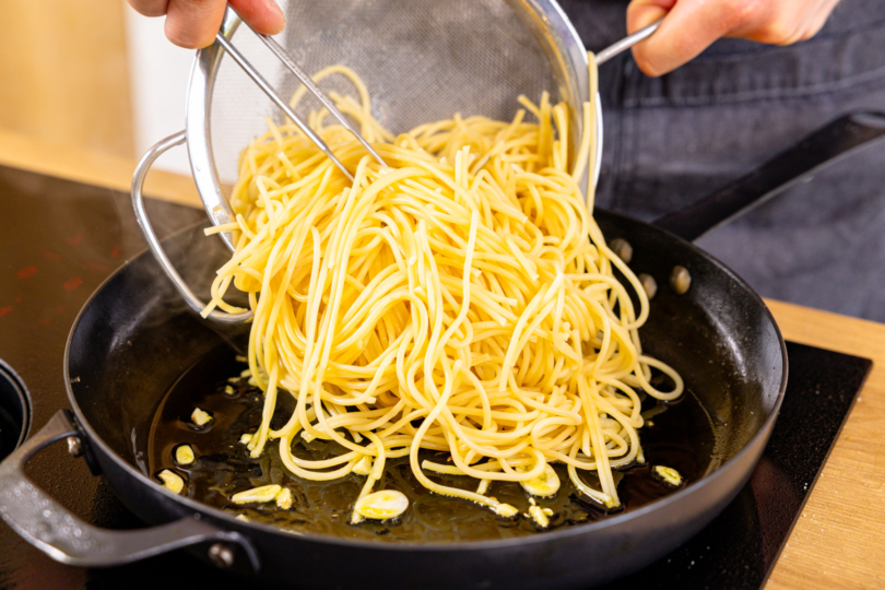 Spaghetti zum Knoblauch in die Pfanne geben