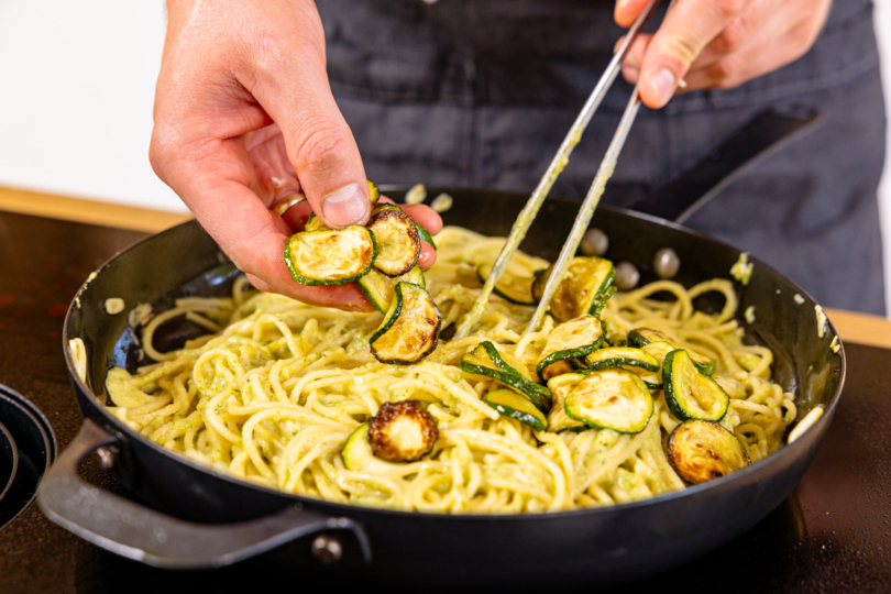 frittierte Zucchinischeiben über Spaghetti geben