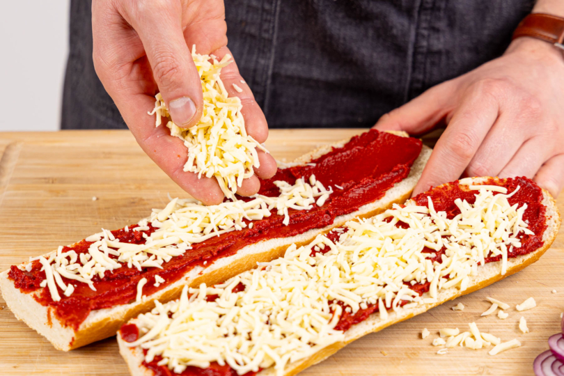 Baguette mit Tomatenmark einstreichen und Käse daraufstreuen