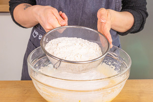 Mehl in die Mischung für den Buttermilchkuchen sieben