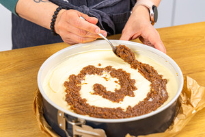Zimtfüllung in Form einer Schnecke auf dem Cinnamon Roll Cheesecake verteilen