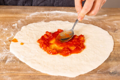 gehackte Tomaten auf Pizzateig verstreichen