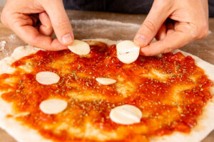 Knoblauchscheiben auf Pizza Marinara verteilen