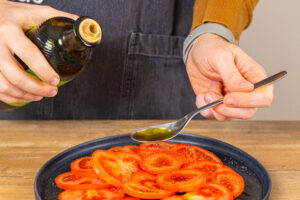 Olivenöl auf Tomatenscheiben geben