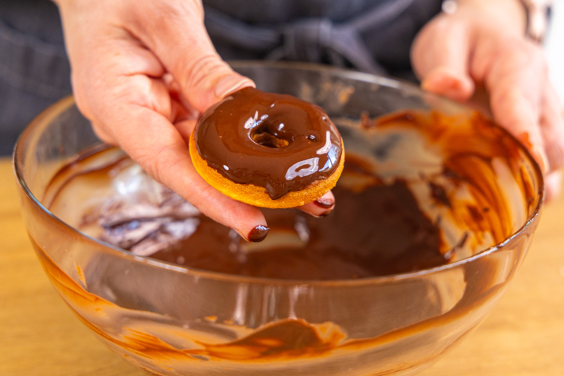 Fertig gebackener Donut in Kuvertüre tauchen