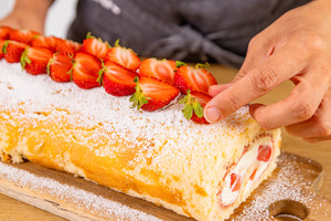 Erdbeer-Biskuitrolle mit frischen Erdbeeren garnieren