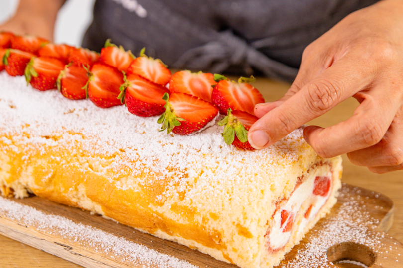 Erdbeer-Biskuitrolle mit frischen Erdbeeren garnieren