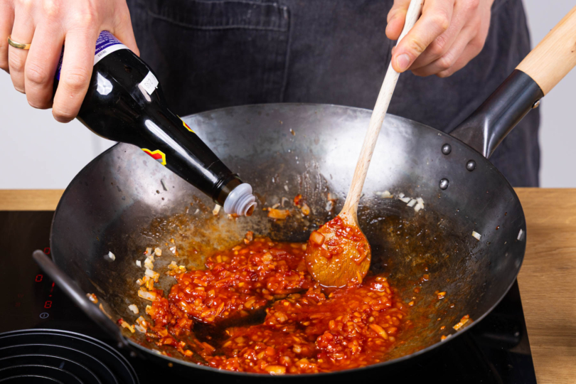 Tomatenmark und Sojasoße in den Wok geben