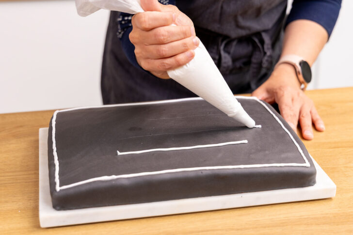 Glasur als Linien auf den Schultafel-Kuchen spritzen