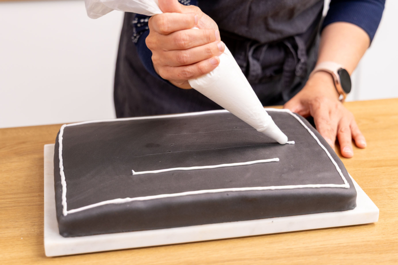 Glasur als Linien auf den Schultafel-Kuchen spritzen