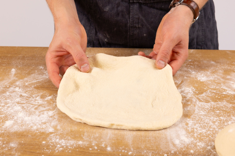 Pizzateig auseinander ziehen.